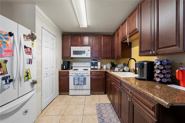 kitchen featuring a textured ceiling, light tile patterned floors, a sink, and white appliances
