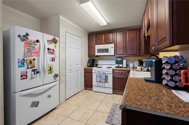 kitchen featuring a textured ceiling, a sink, white appliances, and light tile patterned floors
