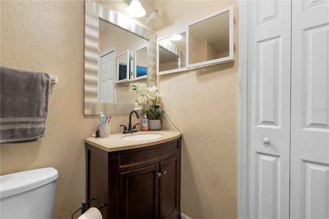 bathroom with a textured wall, vanity, and toilet