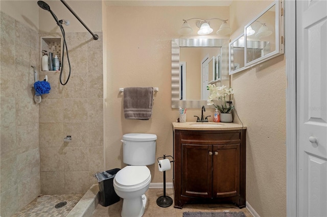 bathroom with tile patterned floors, toilet, a tile shower, baseboards, and vanity