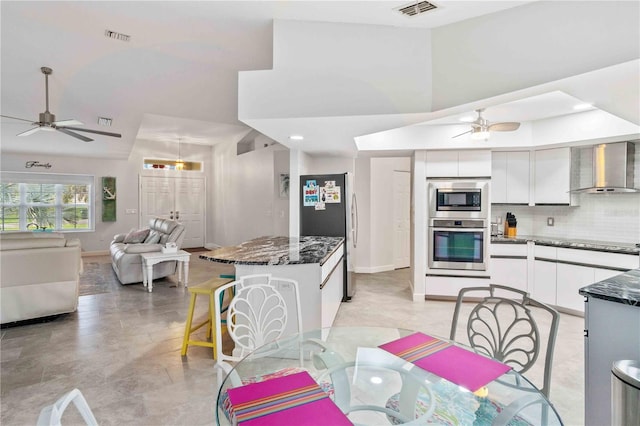 kitchen featuring white cabinets, wall chimney range hood, stainless steel appliances, a kitchen breakfast bar, and backsplash