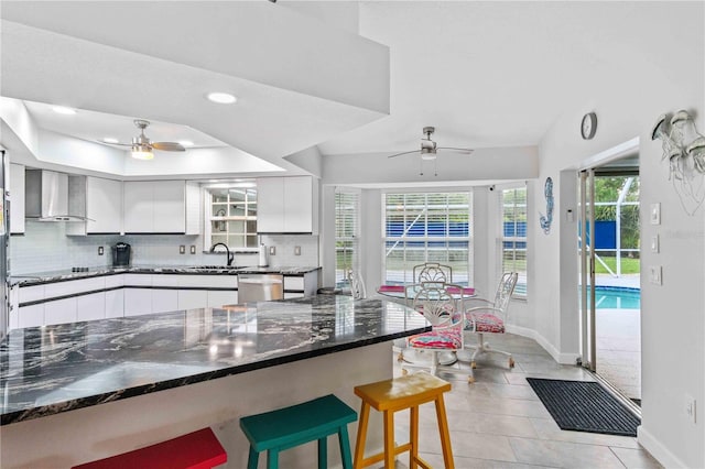 kitchen with ceiling fan, sink, light tile patterned flooring, white cabinetry, and wall chimney exhaust hood