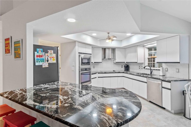 kitchen with white cabinets, wall chimney range hood, stainless steel appliances, dark stone countertops, and sink