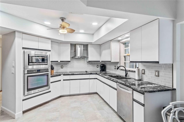 kitchen featuring wall chimney range hood, a raised ceiling, sink, white cabinetry, and stainless steel appliances