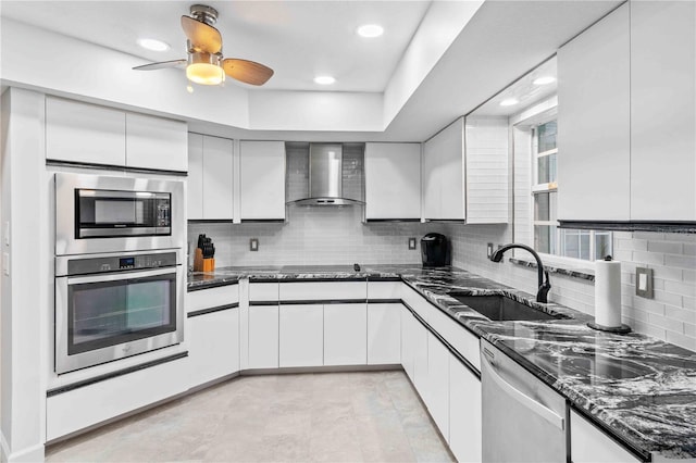 kitchen featuring white cabinets, wall chimney exhaust hood, stainless steel appliances, dark stone counters, and sink