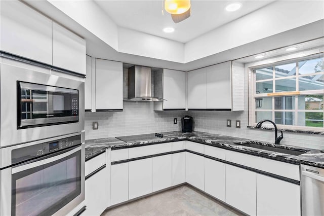 kitchen with decorative backsplash, appliances with stainless steel finishes, wall chimney exhaust hood, and white cabinetry