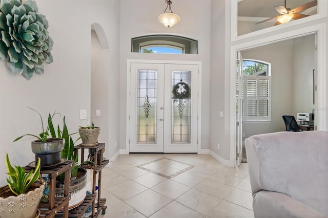 foyer with french doors, a towering ceiling, ceiling fan, and light tile patterned floors