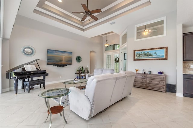 living room featuring light tile patterned floors, ceiling fan, a towering ceiling, ornamental molding, and a raised ceiling