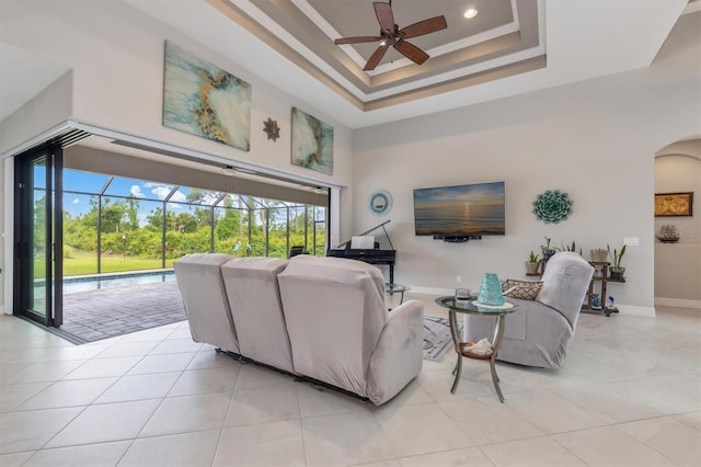 living room featuring a raised ceiling, ornamental molding, light tile patterned floors, and ceiling fan