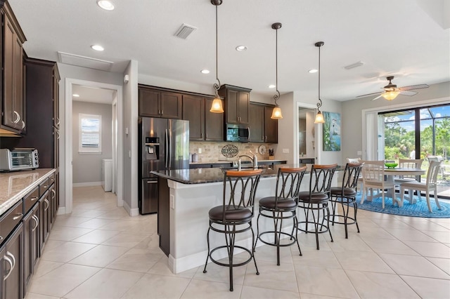 kitchen featuring stainless steel appliances, dark stone countertops, and a center island with sink