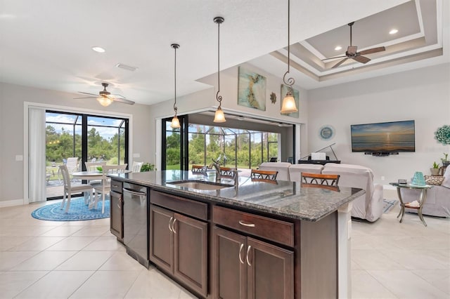 kitchen with pendant lighting, sink, dark stone countertops, dark brown cabinetry, and a raised ceiling