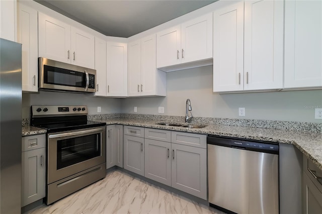 kitchen with gray cabinetry, light stone countertops, sink, white cabinets, and appliances with stainless steel finishes