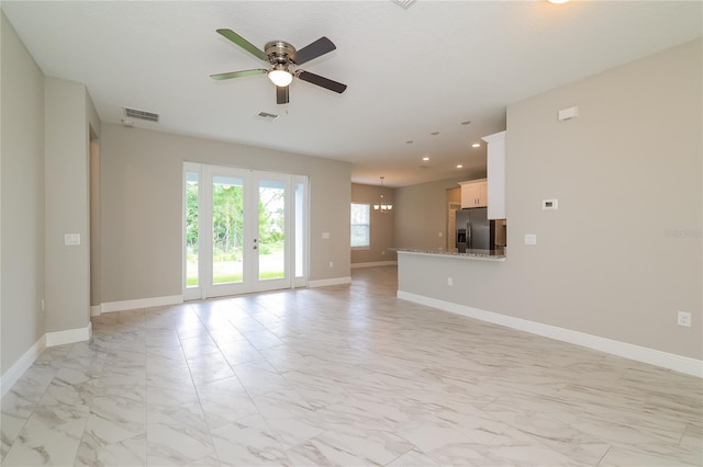 unfurnished living room with french doors and ceiling fan with notable chandelier