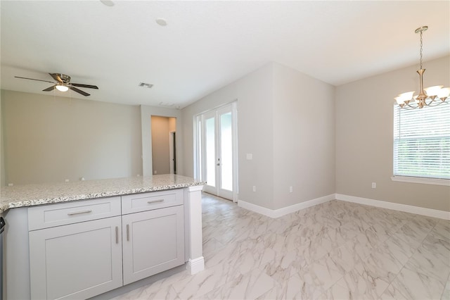 kitchen with light stone countertops, french doors, pendant lighting, and ceiling fan with notable chandelier