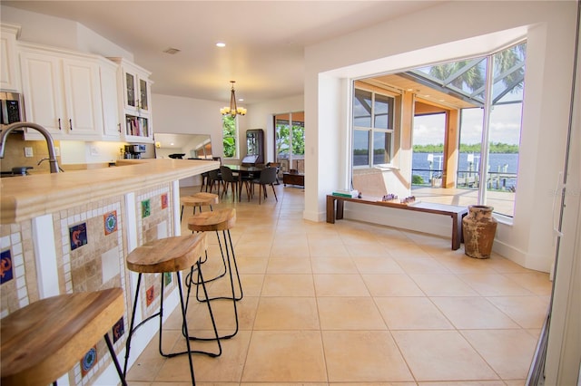 kitchen with pendant lighting, sink, light tile patterned floors, a notable chandelier, and white cabinets