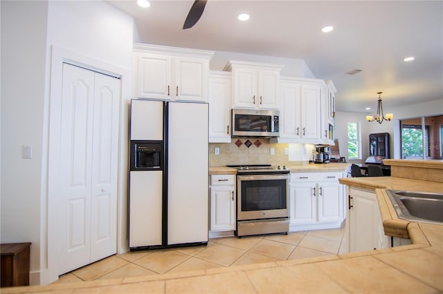 kitchen with decorative light fixtures, light tile patterned floors, appliances with stainless steel finishes, white cabinets, and backsplash