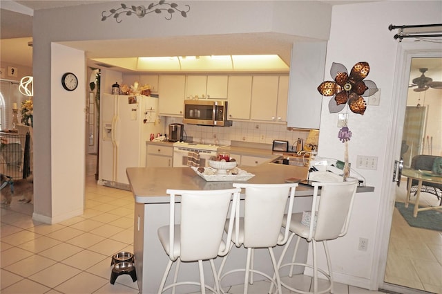 kitchen with white refrigerator with ice dispenser, backsplash, kitchen peninsula, stove, and light tile patterned floors