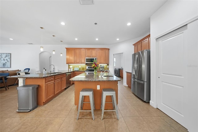 kitchen featuring a breakfast bar, a center island with sink, hanging light fixtures, dark stone countertops, and appliances with stainless steel finishes