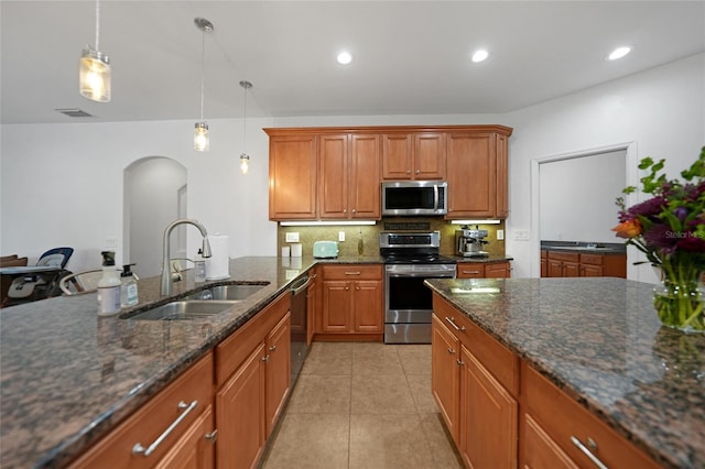 kitchen with appliances with stainless steel finishes, sink, decorative light fixtures, dark stone countertops, and light tile patterned flooring