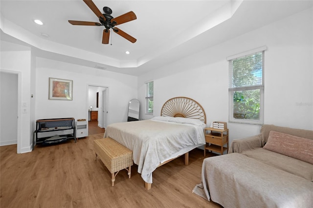 bedroom with a raised ceiling, ceiling fan, and light wood-type flooring