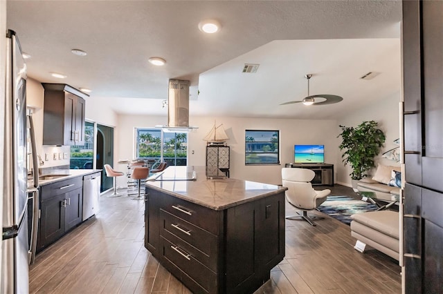 kitchen featuring a center island, stainless steel dishwasher, ceiling fan, light stone countertops, and dark brown cabinets