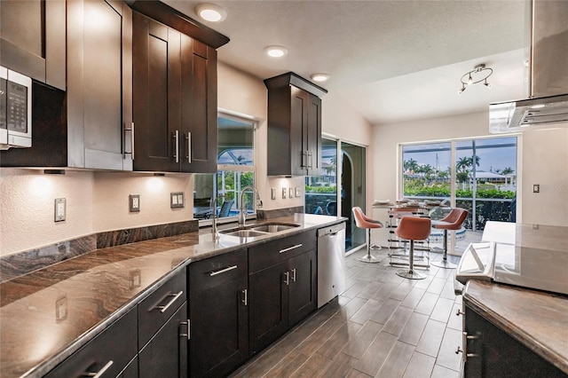 kitchen with stone countertops, sink, vaulted ceiling, stainless steel dishwasher, and dark brown cabinets