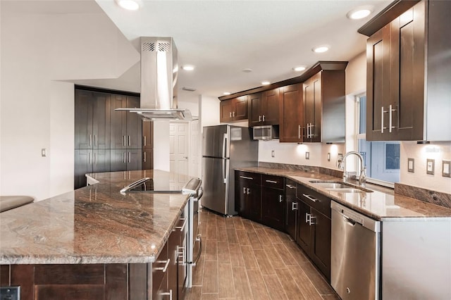 kitchen with a center island, dark stone counters, sink, island range hood, and stainless steel appliances