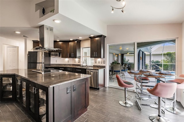 kitchen with island exhaust hood, dark stone countertops, dark brown cabinets, a kitchen island, and appliances with stainless steel finishes