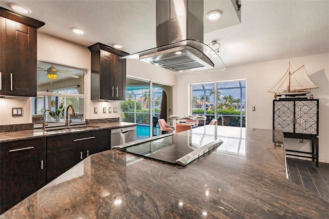 kitchen with stainless steel dishwasher, dark brown cabinetry, island range hood, sink, and dark stone countertops