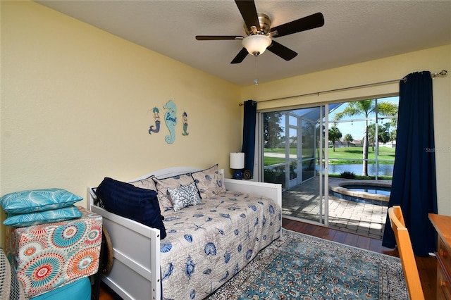 bedroom with hardwood / wood-style flooring, ceiling fan, access to exterior, a water view, and a textured ceiling