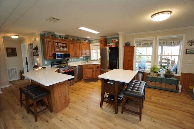 kitchen with a healthy amount of sunlight, kitchen peninsula, light hardwood / wood-style floors, a breakfast bar area, and appliances with stainless steel finishes