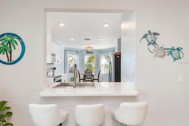 kitchen with kitchen peninsula, tasteful backsplash, stainless steel appliances, sink, and white cabinets