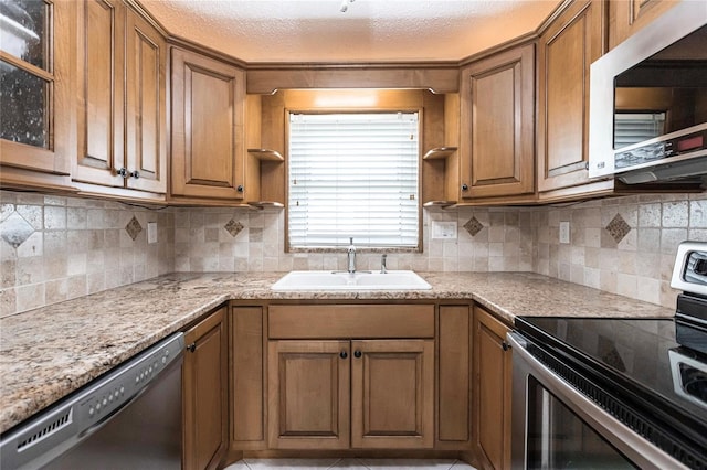 kitchen featuring appliances with stainless steel finishes, decorative backsplash, sink, light stone countertops, and a textured ceiling