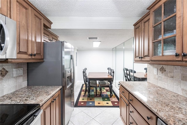 kitchen featuring a textured ceiling, range, light tile patterned floors, and tasteful backsplash