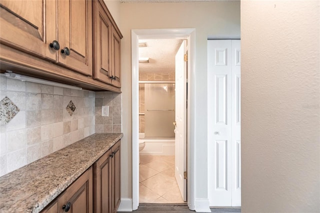 kitchen featuring tile patterned floors, tasteful backsplash, a textured ceiling, and light stone counters