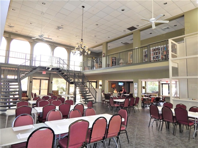 dining area featuring ceiling fan with notable chandelier, a high ceiling, and a drop ceiling