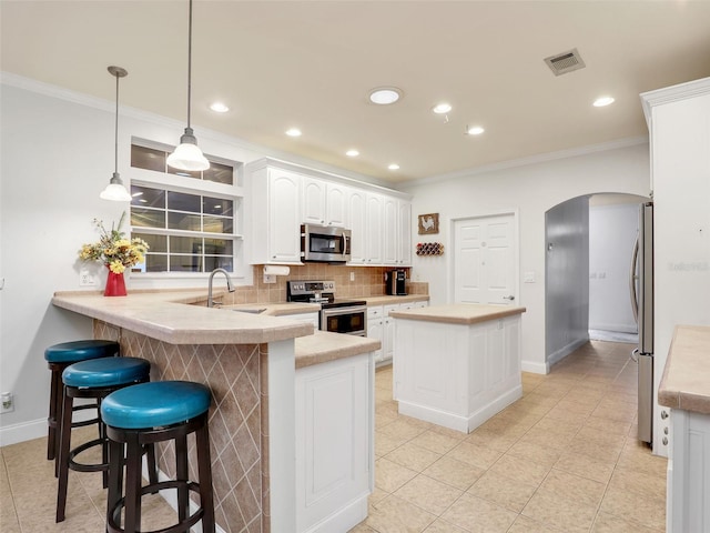 kitchen with white cabinetry, decorative light fixtures, ornamental molding, kitchen peninsula, and stainless steel appliances