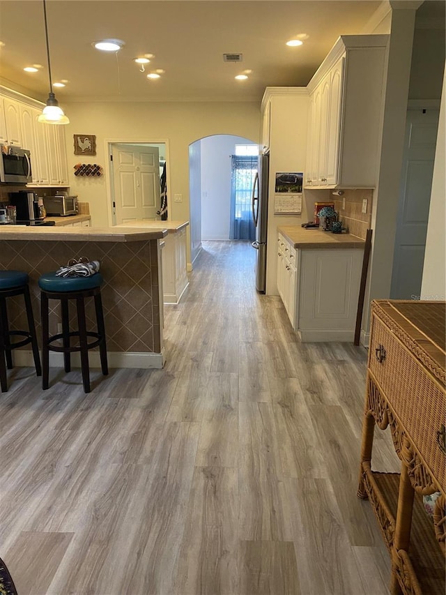 kitchen featuring light wood-style flooring, a breakfast bar, stainless steel appliances, visible vents, and arched walkways