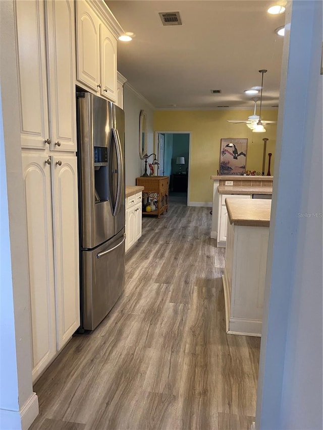 kitchen with wood finished floors, visible vents, stainless steel fridge, white cabinets, and baseboards