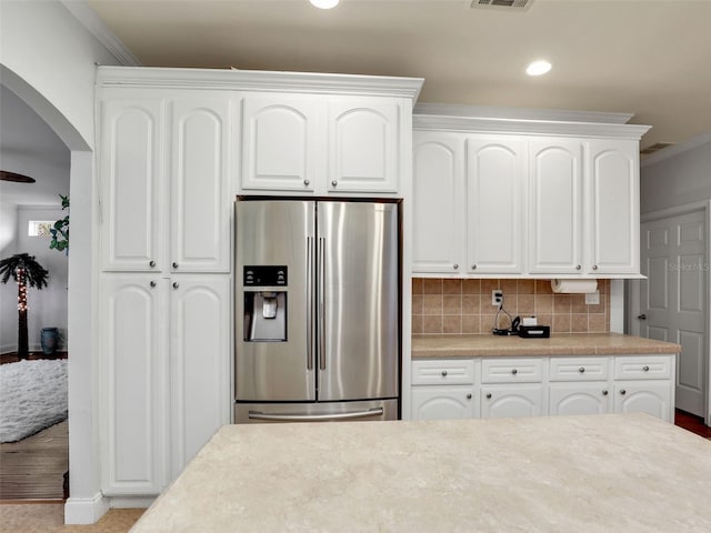 kitchen with ornamental molding, stainless steel fridge, arched walkways, light countertops, and white cabinets