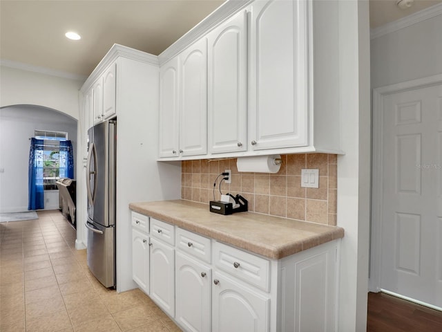 kitchen featuring freestanding refrigerator, crown molding, white cabinetry, arched walkways, and backsplash