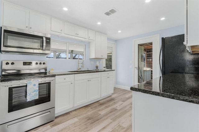 kitchen with sink, stainless steel appliances, light hardwood / wood-style floors, white cabinets, and dark stone counters