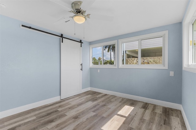 empty room with a barn door, ceiling fan, and light hardwood / wood-style flooring