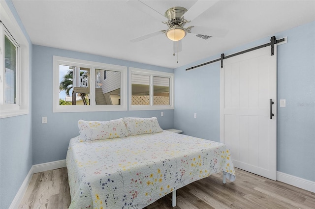 bedroom featuring ceiling fan, a barn door, and light wood-type flooring