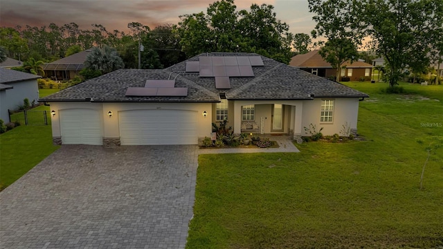 view of front of house featuring a garage, a lawn, and solar panels