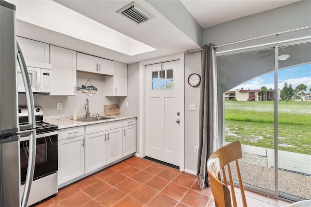 kitchen featuring light tile patterned floors, appliances with stainless steel finishes, white cabinets, and sink