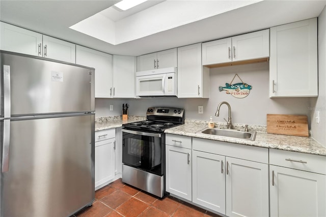 kitchen with appliances with stainless steel finishes, sink, light stone counters, and white cabinetry