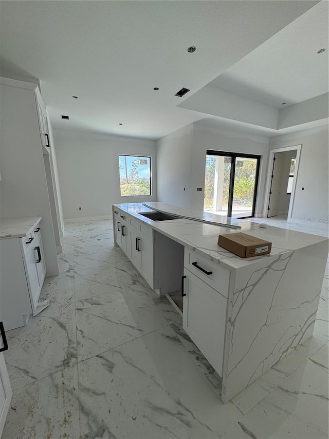 kitchen featuring black electric cooktop, light stone countertops, a kitchen island, and white cabinets