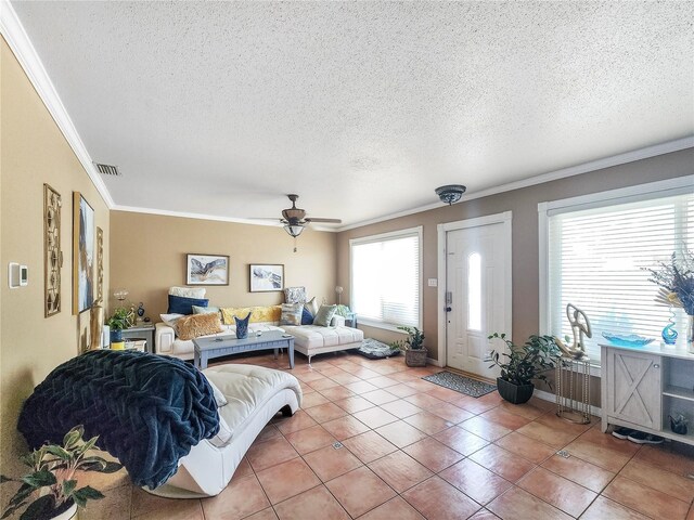 tiled living area with visible vents, ornamental molding, ceiling fan, a textured ceiling, and baseboards