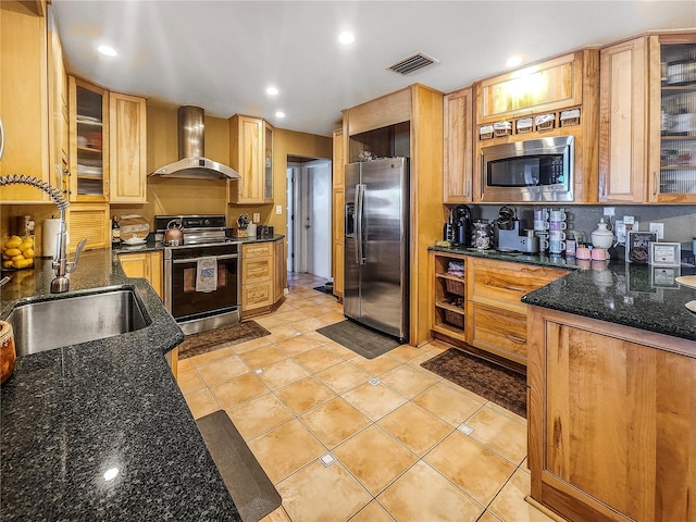 kitchen with stainless steel appliances, sink, light tile patterned floors, dark stone countertops, and wall chimney exhaust hood